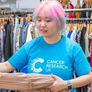 Shop volunteer in front of a rail of clothes, holding a dress