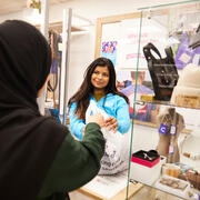 Two people at the till point of a Cancer Research UK shop. One is handing the other a carrier bag.